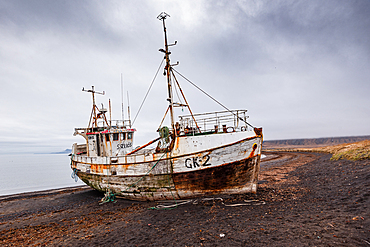 The derelict fishing trawler S&aelig;li&oacute;s, registration GK-2, rusting on the black shore at Rif, Sn&aelig;fellsnes Peninsula, West Iceland, its masts and rigging still intact against a cloudy sky.