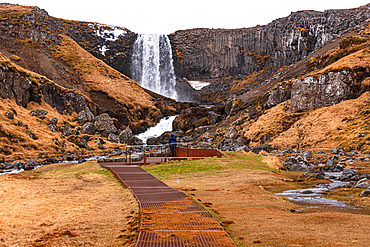 The wooden viewing platform and boardwalk path lead the eye toward Sv&ouml;&eth;ufoss waterfall tumbling between dark basalt column walls at the end of the canyon, near Rif, Sn&aelig;fellsnes Peninsula, West Iceland.