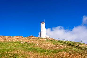 Reykjanesviti lighthouse, Iceland's oldest lighthouse, on green and lava hillside under vivid blue summer sky, Reykjanesta, Reykjanes Peninsula, Iceland.