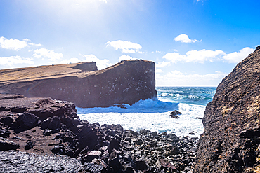 Sheer basalt headland with turquoise Atlantic Ocean surging into narrow channel below, Valahnukamol, near Reykjanesviti lighthouse, Reykjanes Peninsula, Iceland.