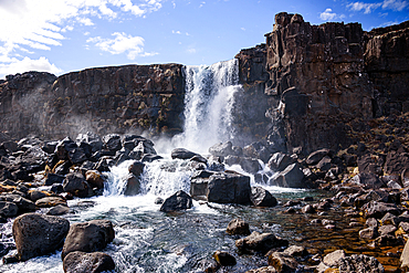 &Ouml;xar&aacute;rfoss waterfall cascading over dark basalt cliffs into a rocky river, &THORN;ingvellir National Park, Iceland. Dramatic Golden Circle landmark framed by towering rift gorge walls.