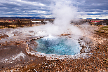 Vivid blue geothermal hot spring with steam rising at Geysir geothermal area, Haukadalur valley, Iceland. Mineral-rich turquoise pool surrounded by golden geothermal sinter, Golden Circle.