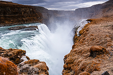 Powerful Gullfoss waterfall cascading over dark tiers into a deep canyon in a swirl of mist, Iceland. Iconic Golden Circle cascade on the glacial Hv&iacute;t&aacute; river.