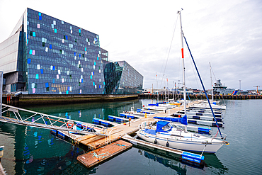 Harpa Concert Hall rising above the old harbour with moored sailing boats, Reykjavik, Iceland. Iconic glass-clad modern architecture on the city's waterfront marina.
