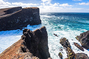 Waves crash on rugged black cliffs with turquoise surf on the Reykjanes Peninsula in Iceland