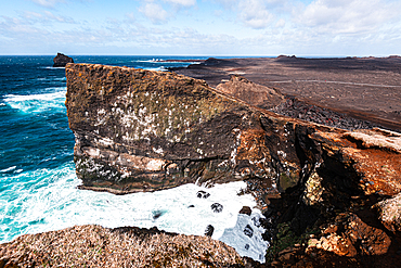 Rugged black lava cliffs rise sharply above turquoise waves on the volcanic coastline at Valahnkaml in Iceland