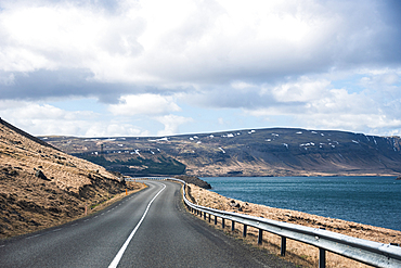 Exploring the open road along a golden hillside with views of the blue fjord and mountains in West Iceland