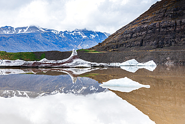 Sv&iacute;nafellsj&ouml;kull glacier and meltwater lagoon, Vatnaj&ouml;kull National Park, South Iceland. Ice floes and a dark ridge reflect across the still lagoon below the ice tongue under a bright cloudy sky. Reflection, glacial retreat, wilderness.