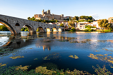 The Pont Vieux and Cath&eacute;drale Saint-Nazaire in B&eacute;ziers, H&eacute;rault, Occitanie, France. The medieval bridge and cathedral hill reflect in the calm Orb in warm daylight.