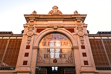 The entrance to Les Halles de Béziers, Hérault, Occitanie, France. The ornate 19th-century covered-market façade rises against a clear blue sky in bright daylight.<br />1372-4479 The entrance to Les Halles de Béziers, Hérault, Occitanie, France. The ornate 19th-century covered-market façade rises against a clear blue sky in bright daylight.