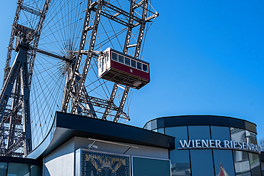 Vienna, Austria &ndash; A red vintage cabin of the Wiener Riesenrad Ferris wheel suspended in the air, showcasing the historic engineering and the 'Wiener Riesenrad' signage.