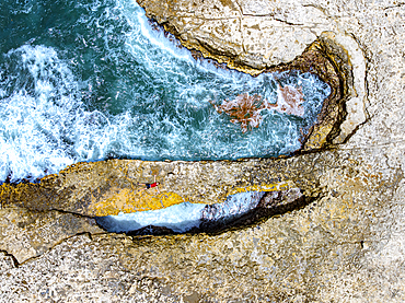 Boy sunbathing on rock arch above ocean waves in Caribbean waters surrounded by natural formations