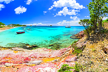 Boat moored in clear waters near sandy beach and rocky shore in Antigua and Barbuda under bright blue sky