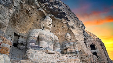 Large statues carved into rock form part of ancient caves with intricate designs at sunset in Shanxi province China
