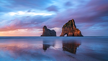 Archway Islands rise from calm waters during sunset at Wharariki Beach in South Island, New Zealand