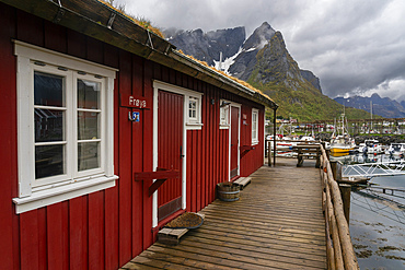 Red building along a wooden dock with boats and mountains in Reine, Lofoten archipelago, Norway