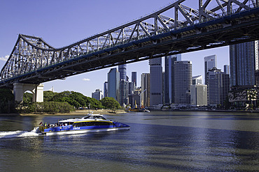 Ferry travels on Brisbane River under Story Bridge with city skyline visible in the background in Queensland, Australia