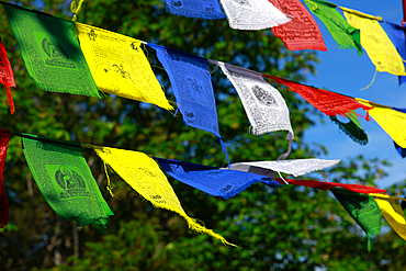 Colorful prayer flags, adorned with mantras and images of deities, flutter in the wind in front of a Tibetan pagoda, symbolizing spirituality and Buddhist tradition.