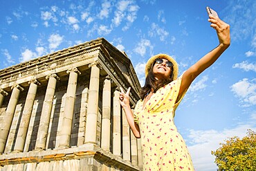 Pretty woman taking selfie in Armenia by Garni roman temple - Happy tourist having fun walking outside on summer vacation - Travel, holidays and European landmarks concept