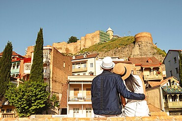 Couple of tourists in street hug enjoy beautiful Tbilisi old city colorful buildings at holidays in Georgia, caucasus. Romantic couple get away together on summer vacation .People and holidays concept