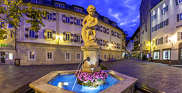 Fountain in Stadtplatz during dusk with a sculpture, flowers, and buildings in Zell am See
