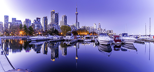 View of CN Tower and city skyline at dusk from Spadina Quay with boats in the foreground in Toronto