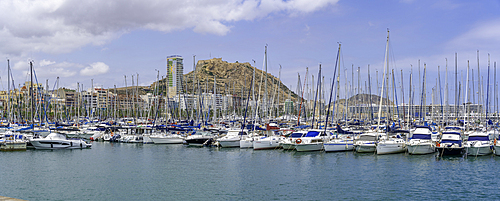 Boats in Alicante Marina with Castillo de Santa Barbara in the background under a sunny sky in Costa Blanca, Spain