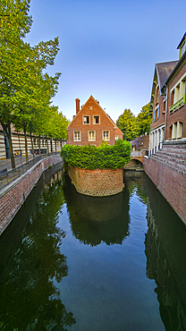 Small channel flows through trees near house in Amiens, France on a clear day with blue sky