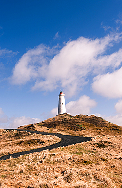 Reykjanesviti lighthouse, Iceland's oldest lighthouse, on rocky headland with winding path under blue sky, Reykjanesta, Reykjanes Peninsula, Iceland.