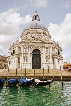 Majestic Venice church with intricate architecture reflects in calm waters. Gondolas line the canal in this breathtaking scene, capturing the essence of Italy's beauty