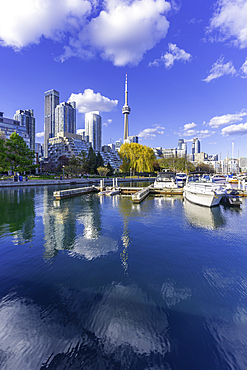 View of CN Tower and city skyline from Spadina Quay on a sunny day with blue skies and boats in water