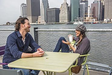 Happy couple sitting and discussing with cityscape in background, Brooklyn, New York