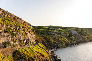 A scenic view of a winding road along a cliff overlooking a calm sea at sunset at Great Orme, in Llandudno, North Wales.