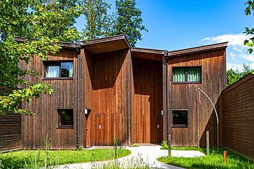 A contemporary house with dark wooden siding, curved walls, and large windows, set in a lush green environment at Center Parcs Villages Nature Paris, France.