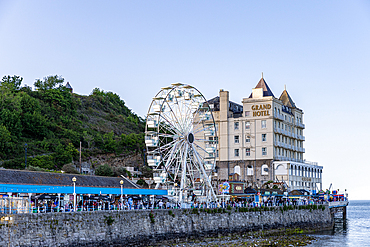 A scenic view of a Ferris wheel beside the Grand Hotel, with a stone wall and a hill in the background in Llandudno, North Wales.
