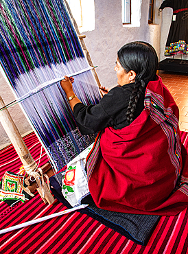 Indigenous woman weaves on a loom while creating traditional textiles in Bolivia