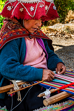 Woman weaves fabric by hand using a loom in a Peruvian village in the Andes mountains during daytime
