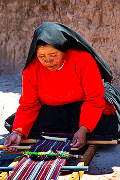 Woman weaving fabric in traditional dress on Taquile Island in Peru near Lake Titicaca