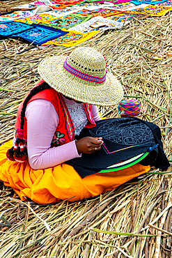 Woman stitching cloth design in traditional style on Uros floating island in Peru's highlands